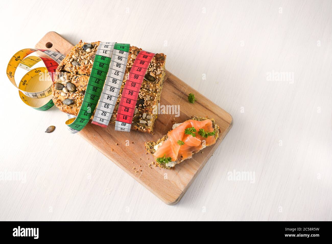 Protein bread with tape measure and a sandwich with salmon on a cutting board and a white table, slimming concept with low carb or ketogenic diet, cop Stock Photo