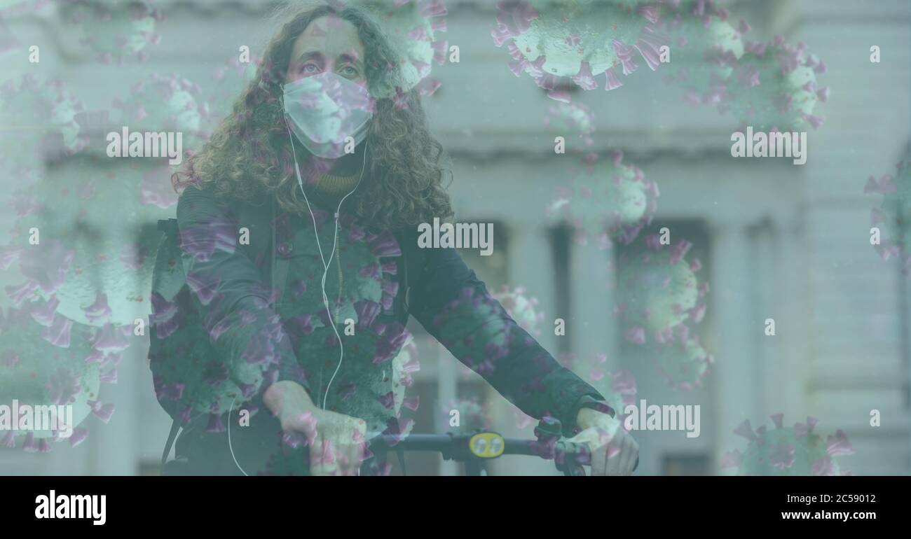 Covid-19 cells against woman wearing face mask riding bicycle Stock Photo