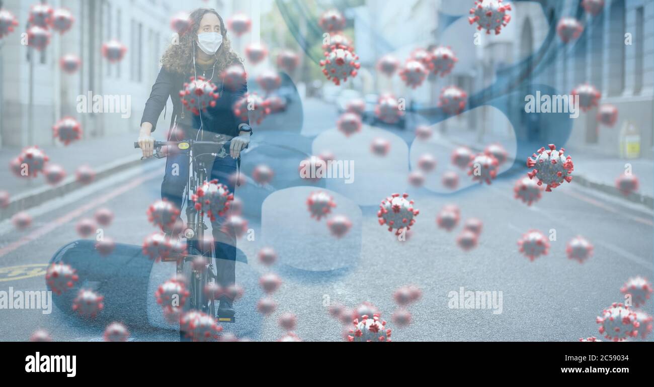 Covid-19 cells against woman wearing face mask riding bicycle on the road Stock Photo