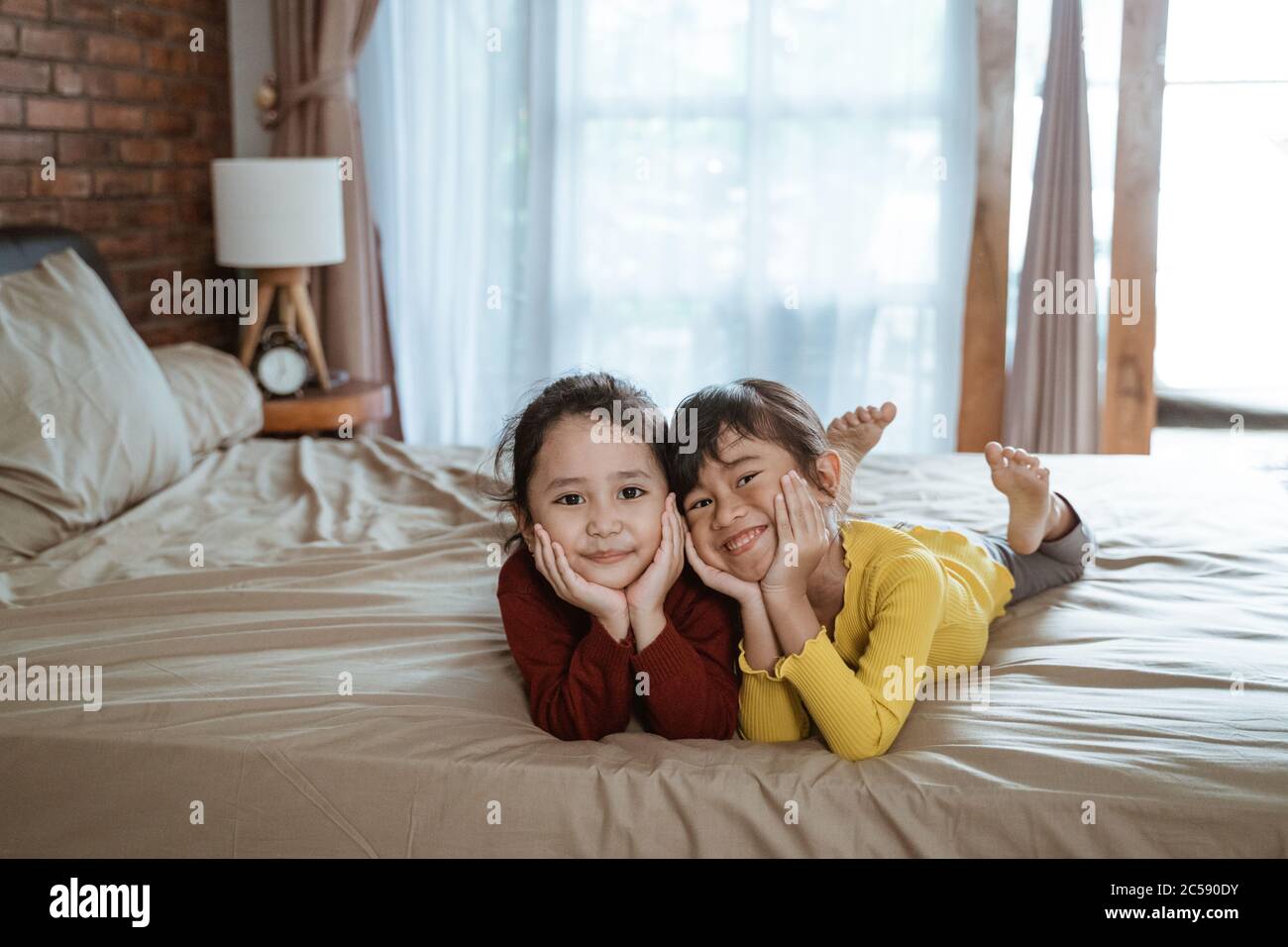 happy two little girls lying on the bed and looking each other in the ...