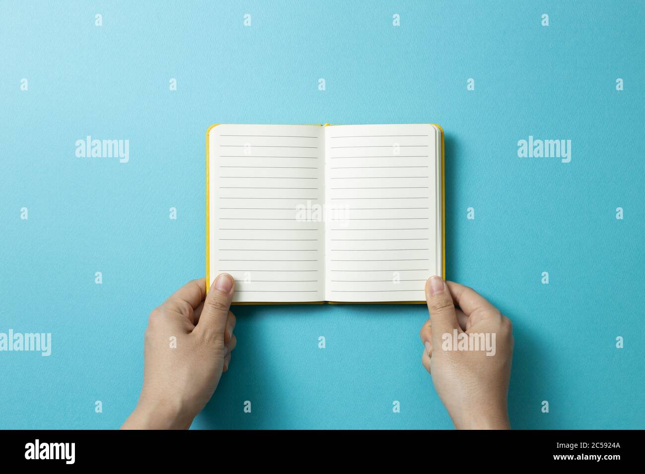 Hands open empty notebook on blue background. top view, copy space Stock Photo