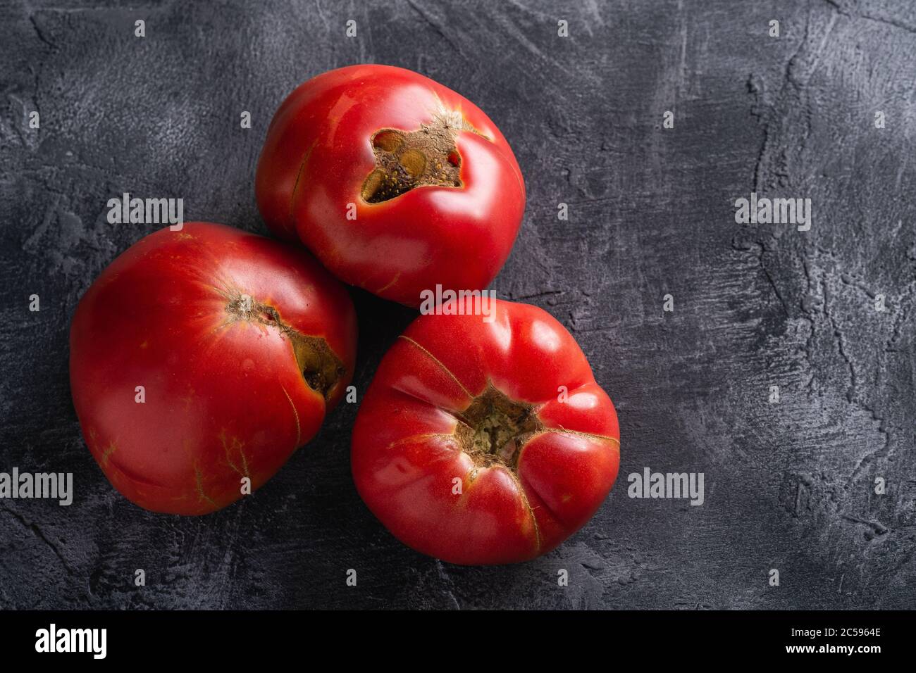 Three pink heirloom tomato vegetables, fresh red ripe tomatoes, vegan food, dark stone concrete background, top view Stock Photo