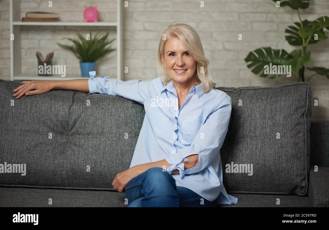 Pretty middle aged woman is sitting on a sofa at home Stock Photo