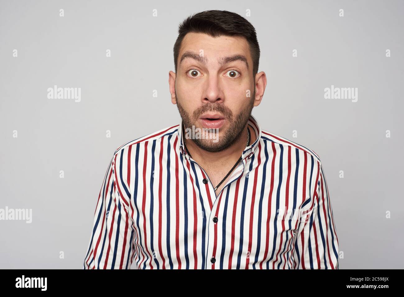 Surprised bearded handsome man wearing striped shirt. Isolated on grey background Stock Photo