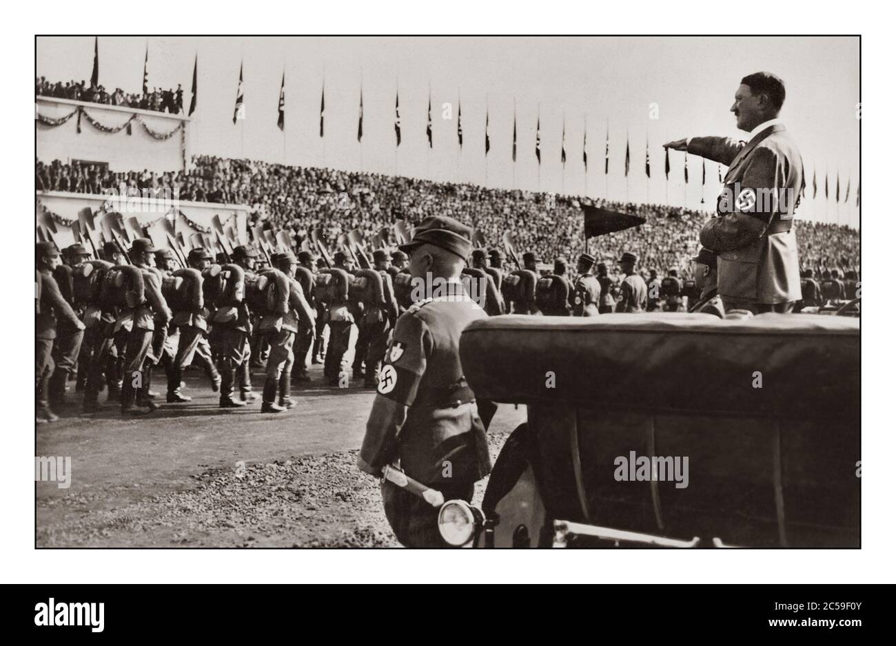 Adolf Hitler wearing a swastika armband at a 1930’s Nazi Party Nuremberg rally, standing in the back of his open top Mercedes motorcar saluting the passing troops of the NSDAP political party military wing Stock Photo