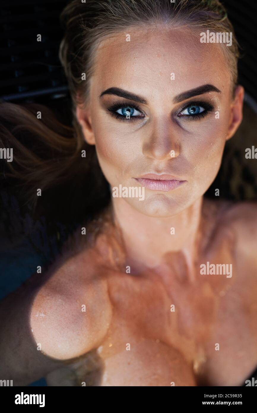 Relaxation and spa concept. Closeup portrait of a sexy fashionable lady in a black swimsuit. Woman with wet hair and makeup poses in water in swimming Stock Photo