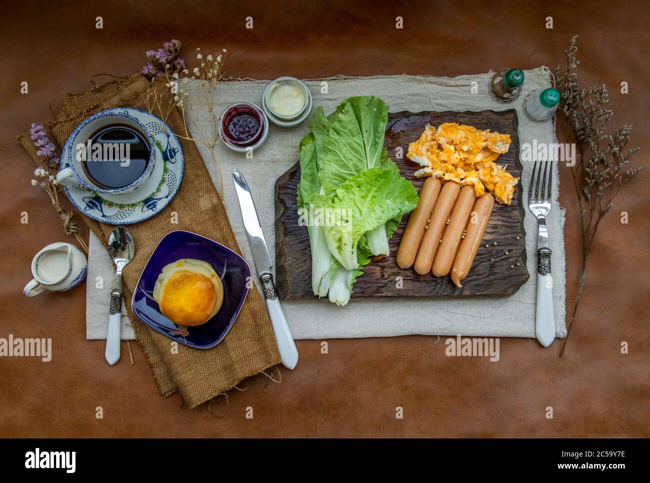 Continental breakfast with scrambled eggs, fried sausages, vegetable and scones served with coffee with milk. Wood background, Selective focuse. Stock Photo