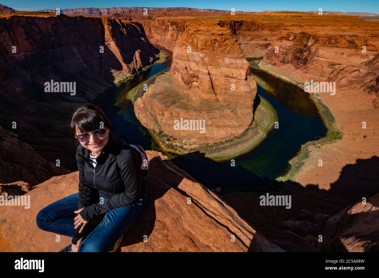 A tourist poses on the Horseshoe Bend overlook of the Colorado River outside of Page, Arizona. Stock Photo