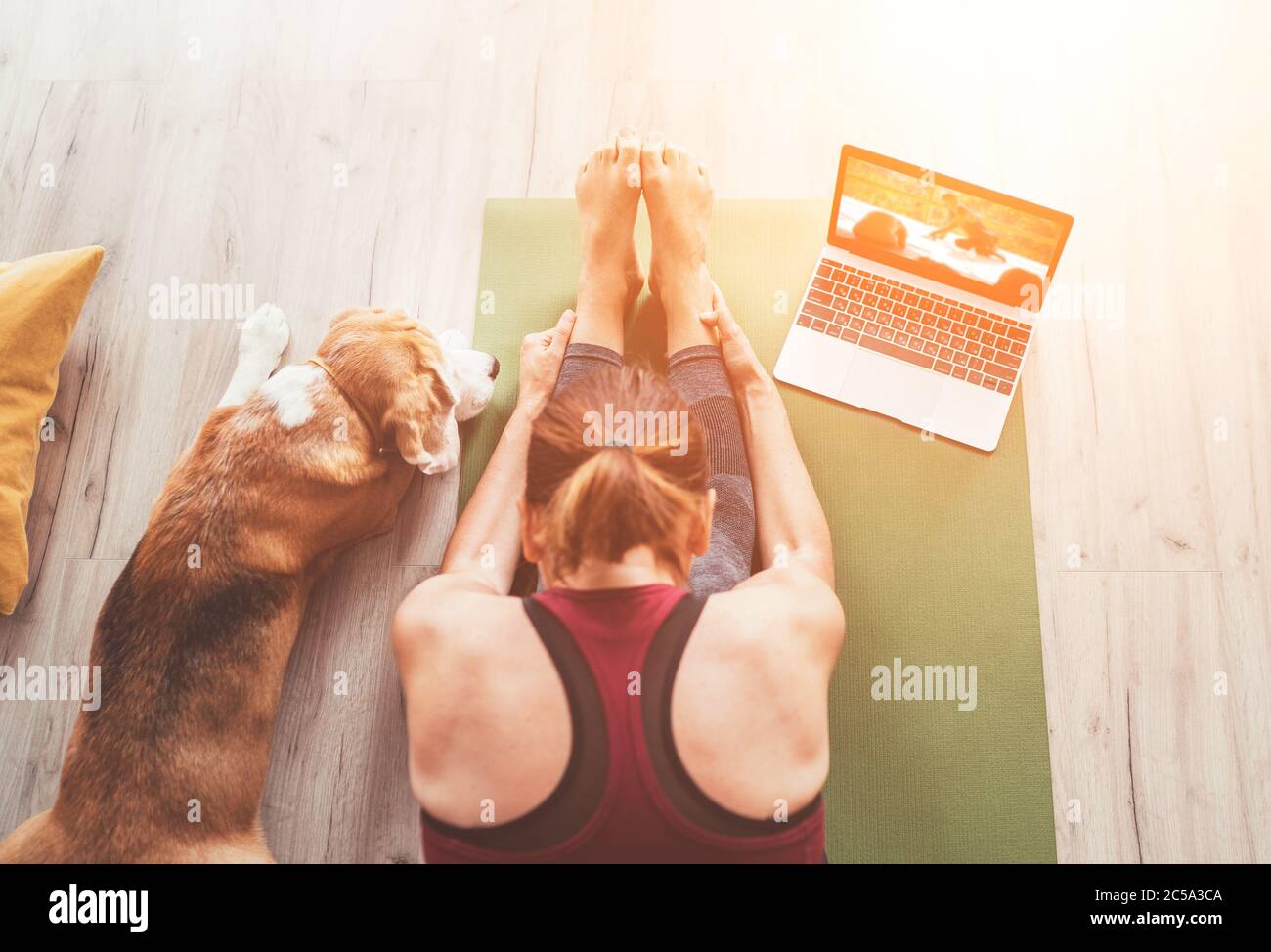 Top view at fit sporty healthy woman sit on mat in Paschimottanasana pose, doing breathing exercises, watching online yoga class on laptop computer. H Stock Photo
