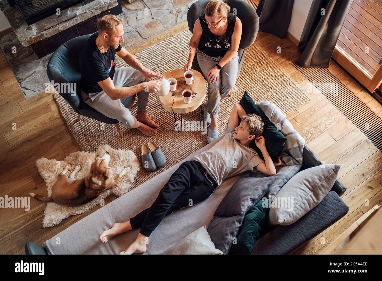 Peaceful family moments concept image. Cozy family drinking tea time. Father, mother and son at the home living room. Boy lying in comfortable sofa an Stock Photo