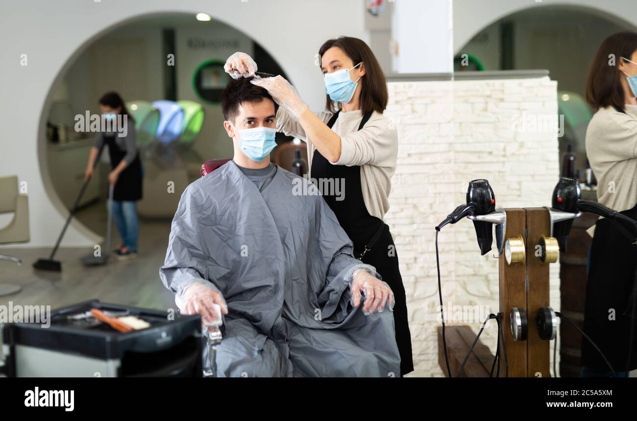 Young woman stylist wearing face mask and gloves working in hairsalon ...