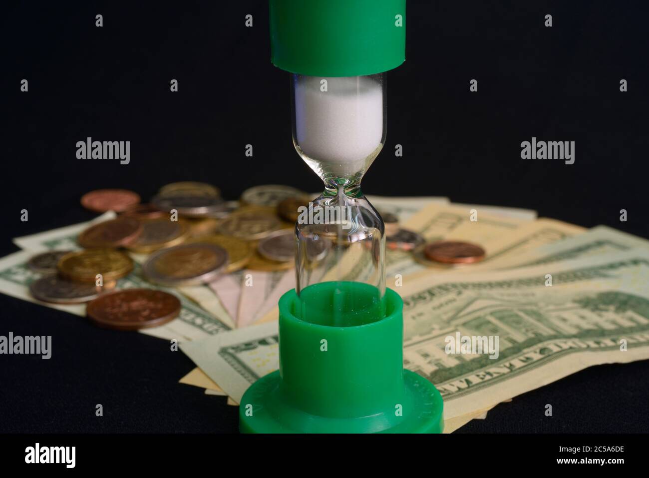 Time is money, do not waste your time: sand flowing in an hourglass, put on the blurred coins and USA banknotes background Stock Photo
