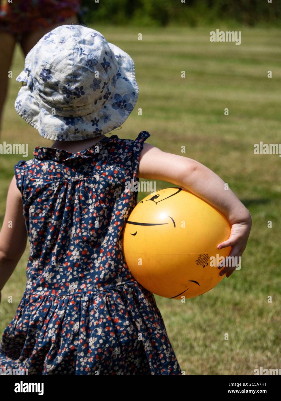Toddler carrying a ball under her arm, UK Stock Photo