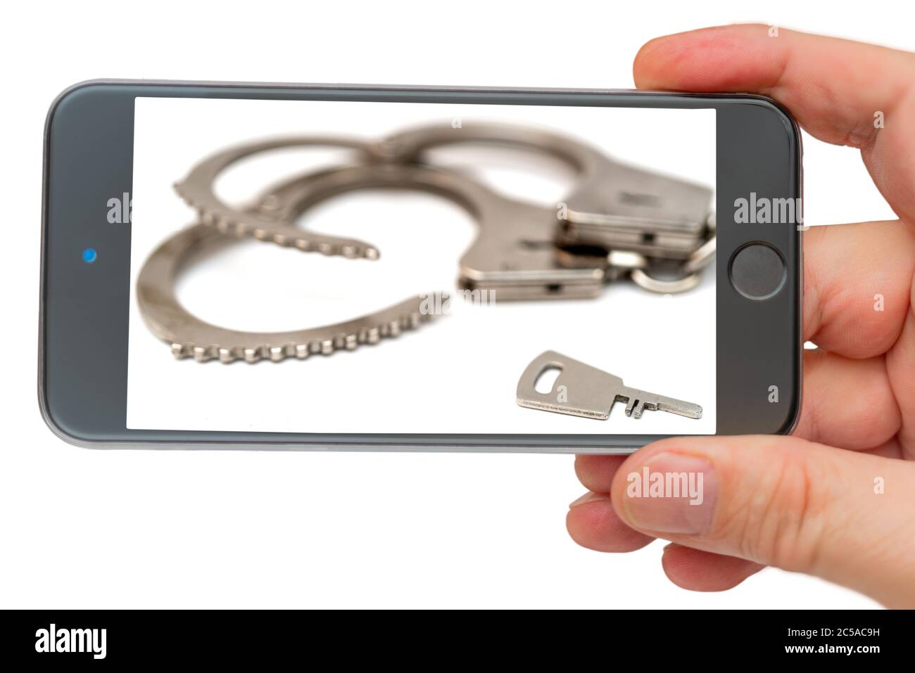 Metal handcuffs on smartphone screen. The detention of criminals breaking the law. Restriction of freedom. Stock Photo