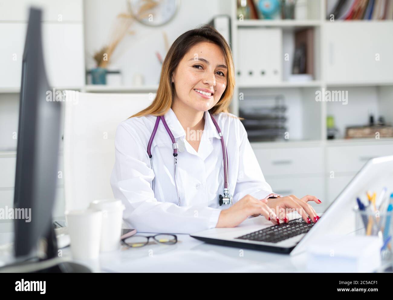 Young hispanic woman doctor assistant working in medical office using ...