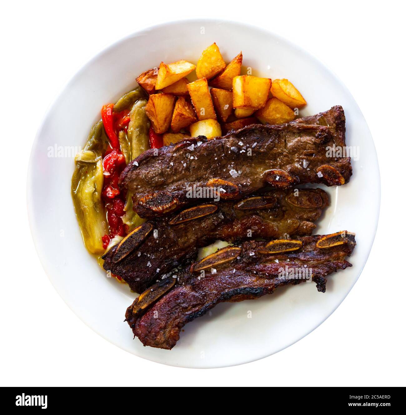 Appetizing grilled beef ribs served on white plate with fried potatoes and baked bell pepper. . Isolated over white background Stock Photo