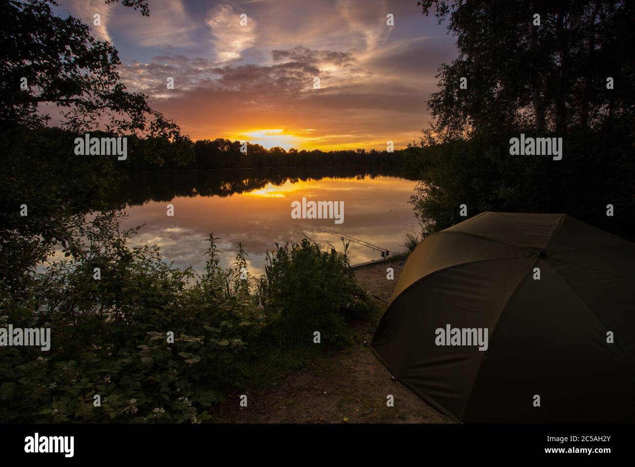 Sunset in the UK over a carp fishing lake. Golden colours with a fishing tent and fishing rods Stock Photo