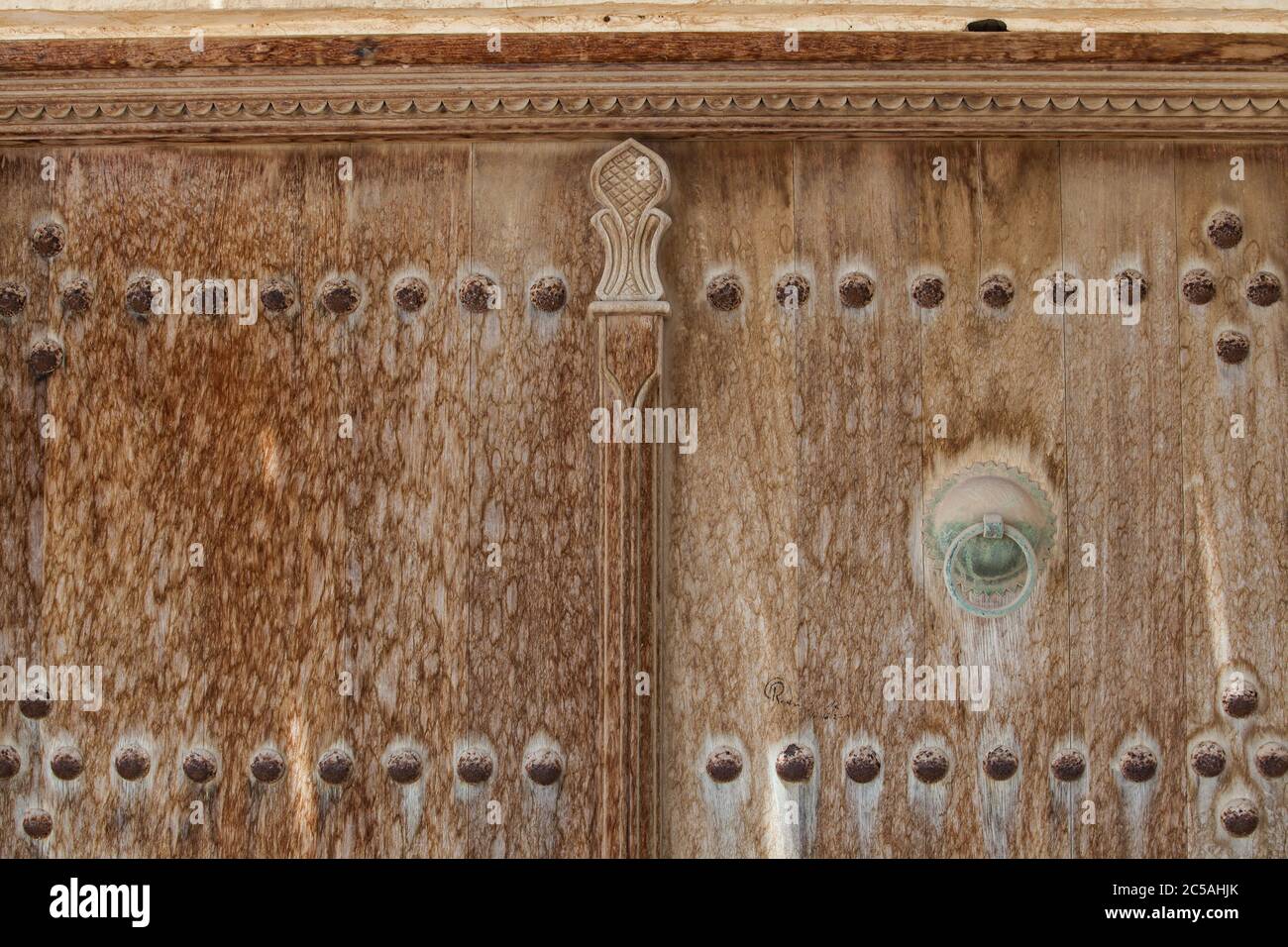 Weathered carved and studded wooden door detail with metal handles