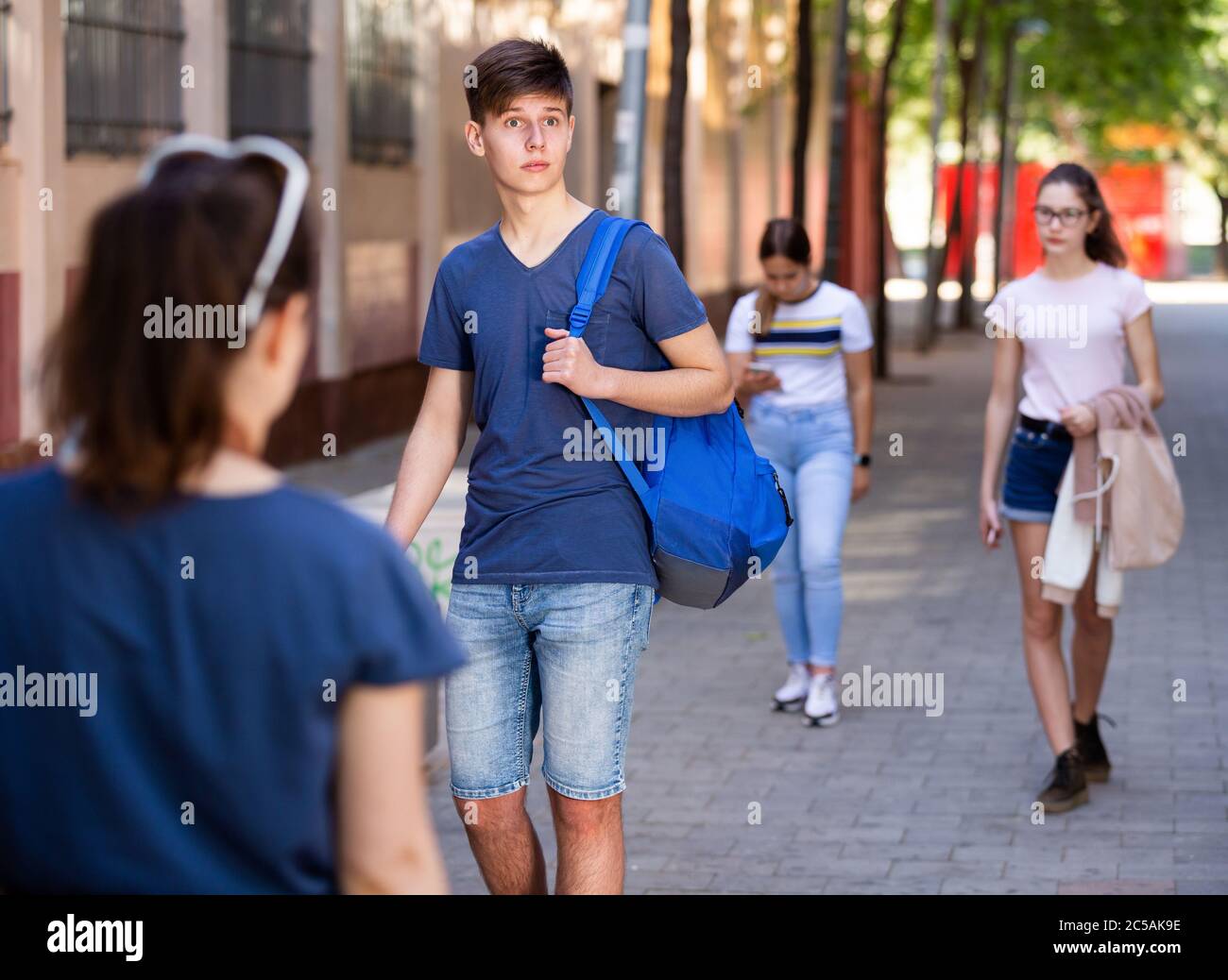 Confident teen boy with backpack strolling through modern city streets on sunny summer day Stock Photo
