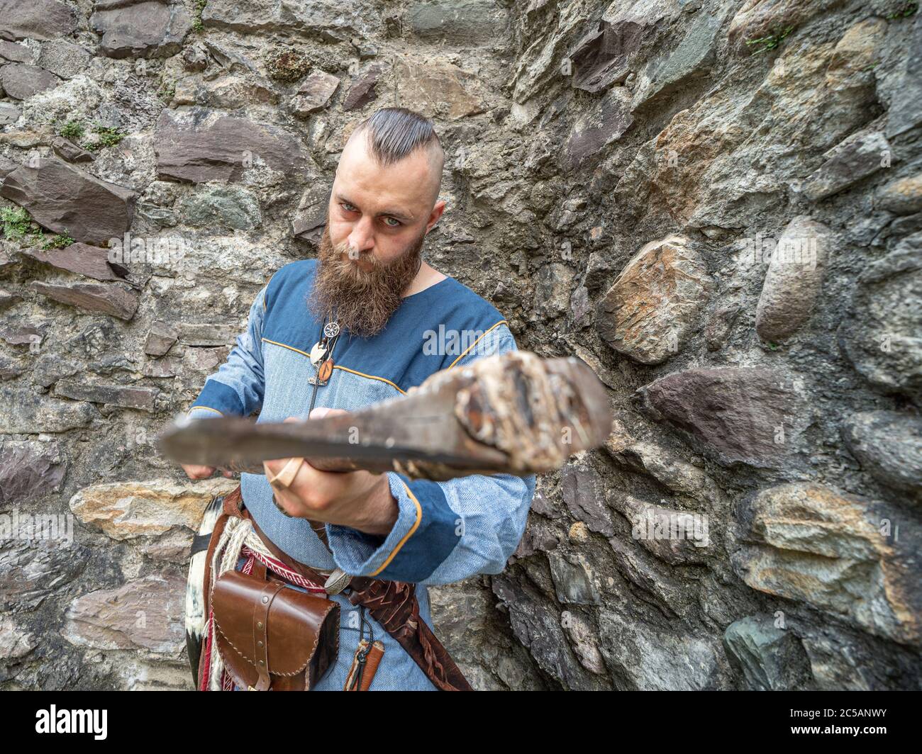 Portrait of a young Viking brandishing an ax in front of a stone wall, portrait set outdoors Stock Photo