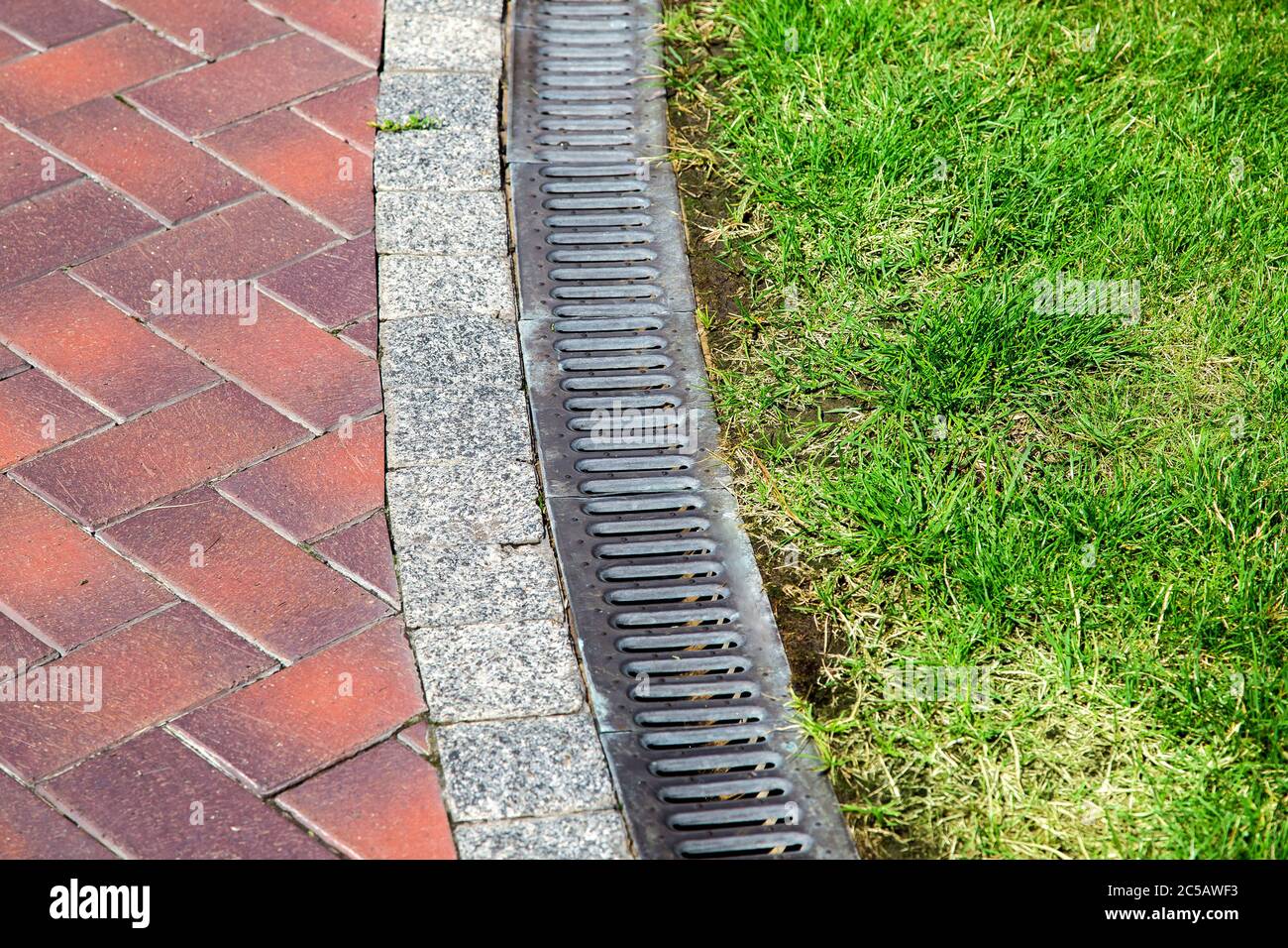 curve iron gutter with grate to the drainage system on the side of the  walkway with green lawn on summer day in well maintained park Stock Photo -  Alamy