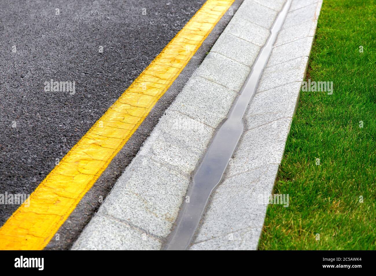 drainage edge tray with stream rain near an asphalt road with a yellow marking and a green lawn after rain Stock - Alamy