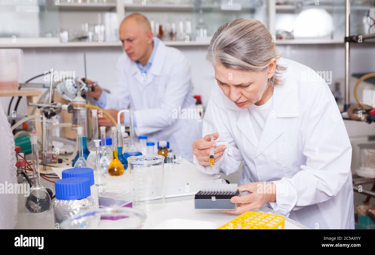 Experienced female biochemists mixing chemicals while performing ...