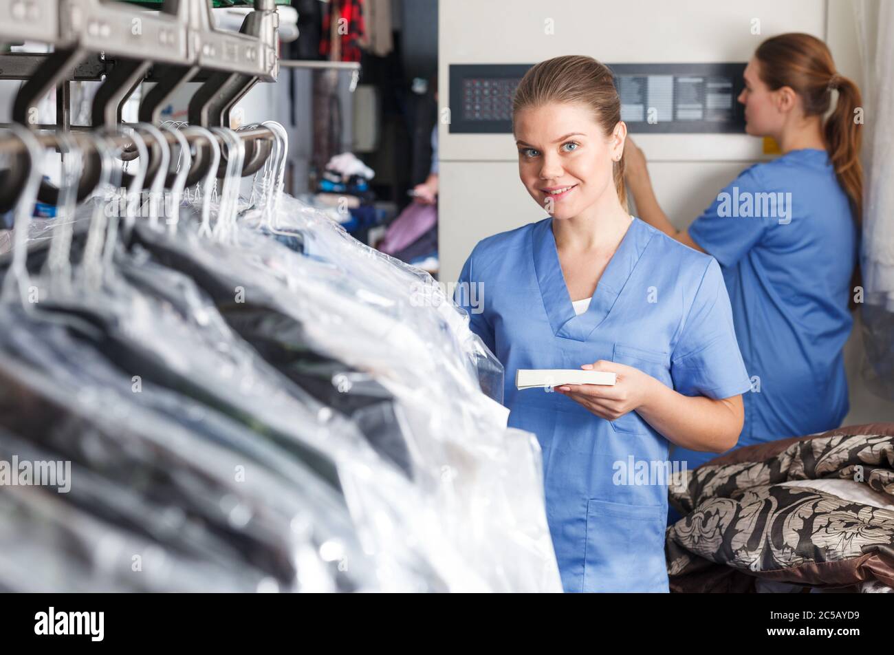 Portrait of girl laundry worker on background of garments racks at dry cleaner Stock Photo