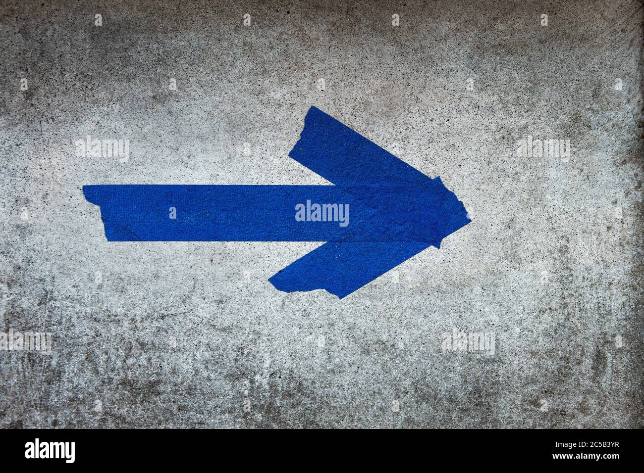 Horizontal shot of an arrow sign made from blue ducktape on a cement wall Stock Photo