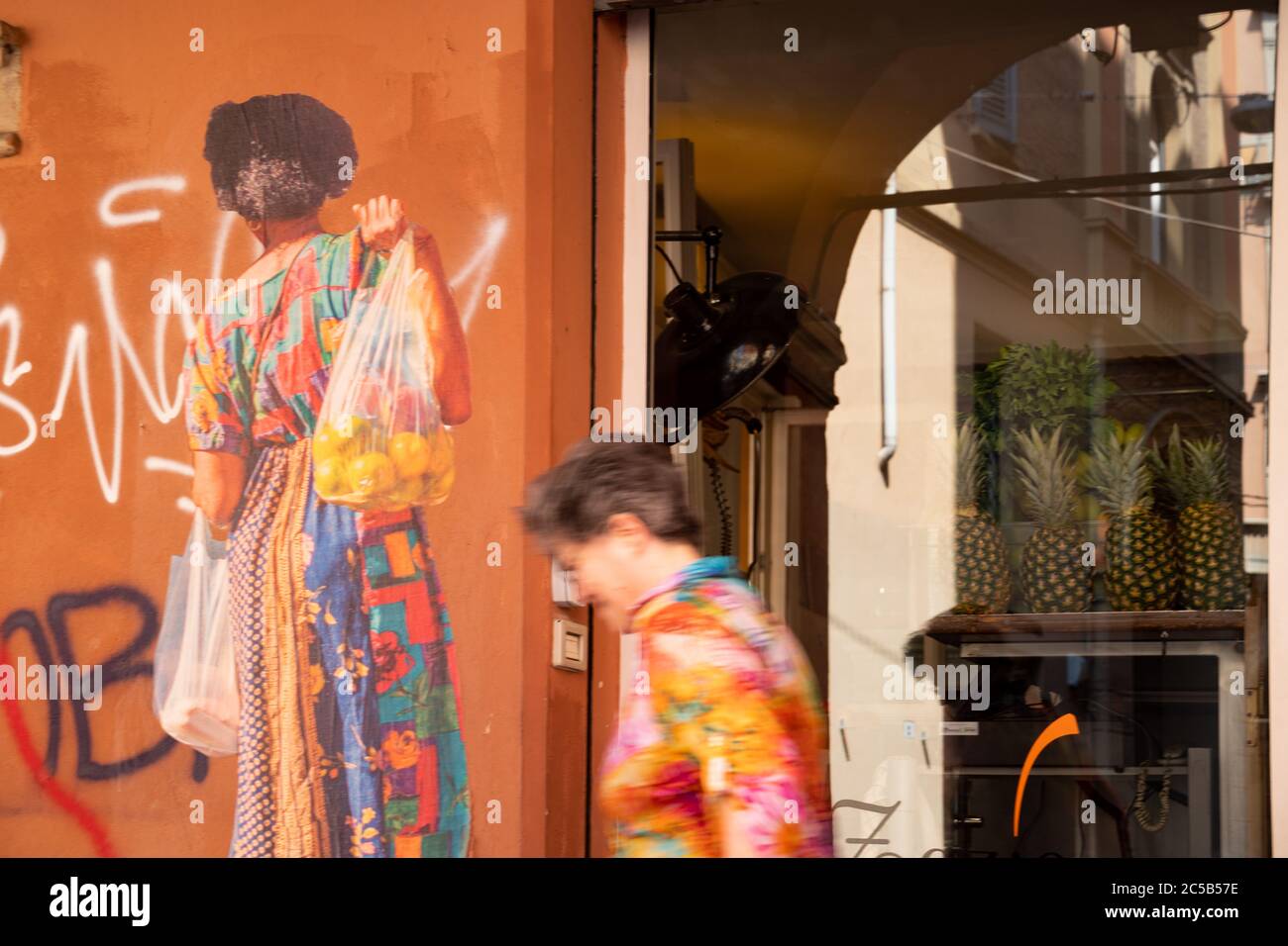 Blurred woman wearing a colorful summer dress passing by on a street of the old city center. Bologna, Italy. Stock Photo