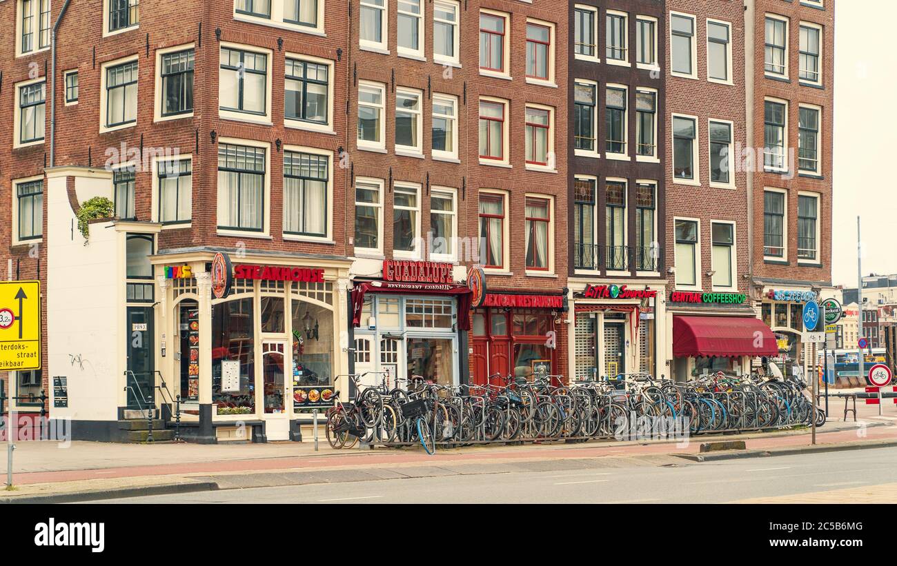 Amsterdam, Netherlands - March 2020 : Amsterdam street panorama with historical buildings, bike parking with many bicycles, restaurants and coffee shop. Stock Photo