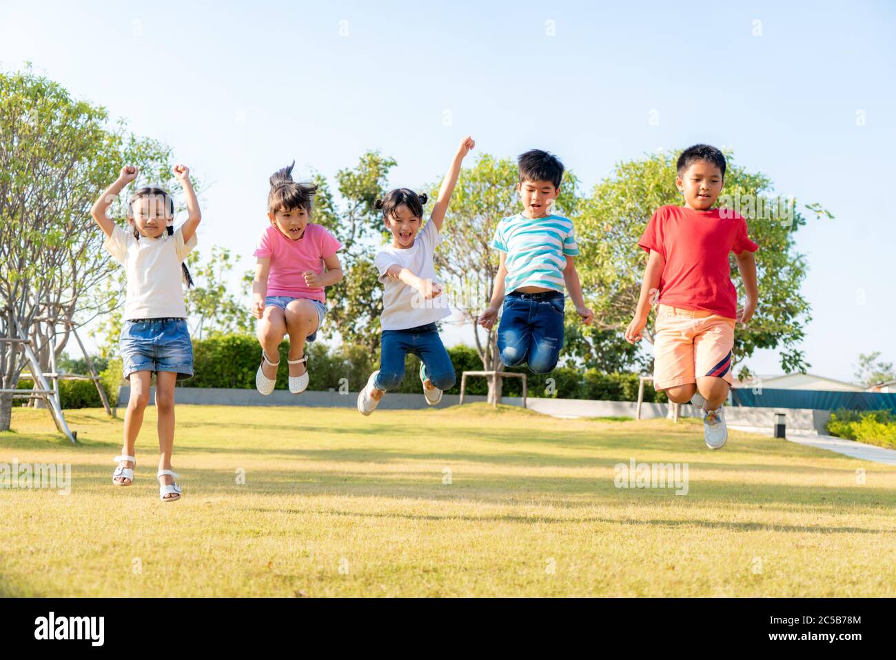 Large group of happy Asian smiling kindergarten kids friends holding hands playing and jumping together during a sunny day in casual clothes at city p Stock Photo