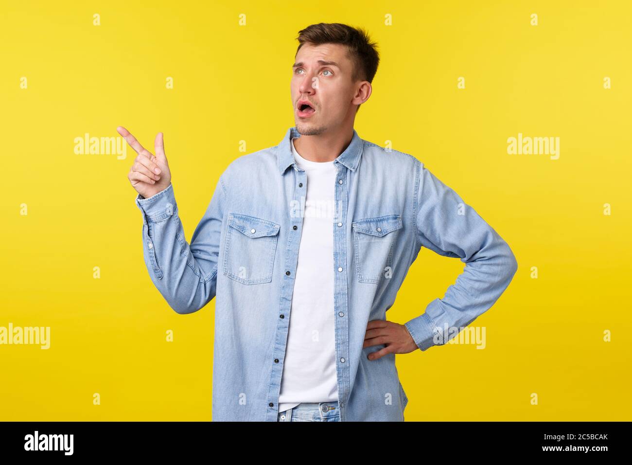 Confused and surprised startled handsome adult man asking question about product, looking and pointing finger upper left corner, consulting shop clerk Stock Photo