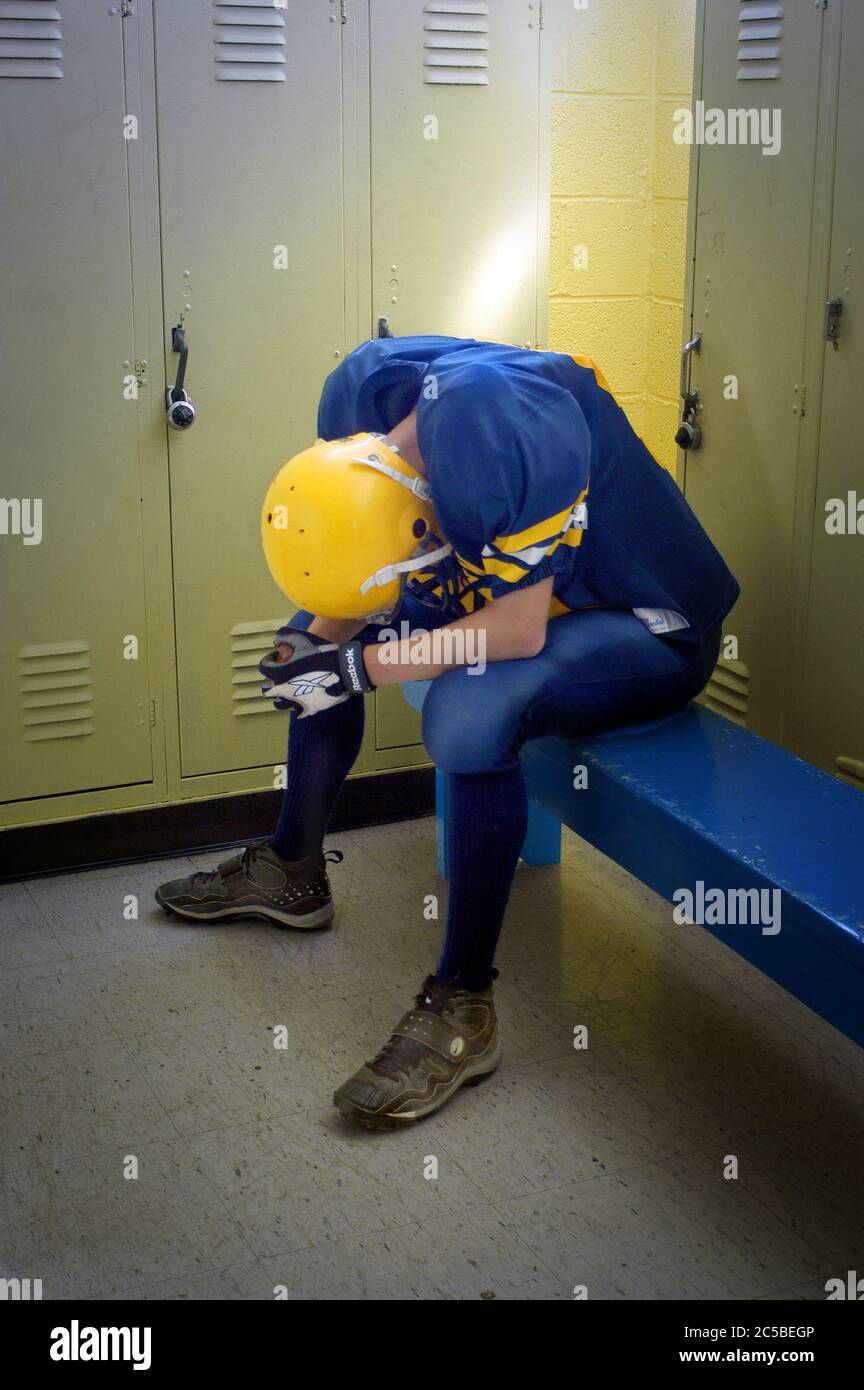 High School Football player sitting alone in depression alone in locker room after defeat Stock Photo