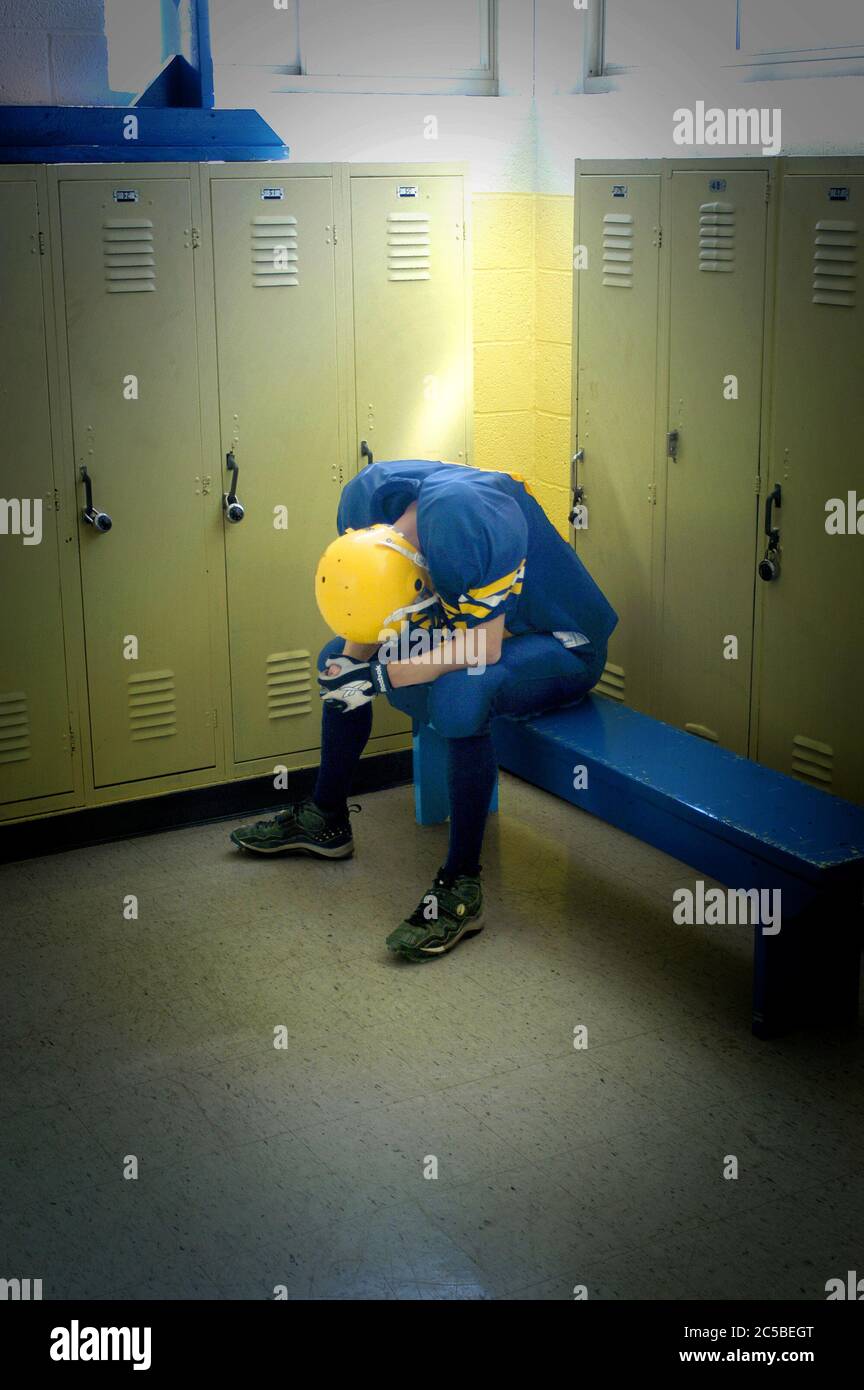 High School Football player sitting alone in depression alone in locker room after defeat Stock Photo