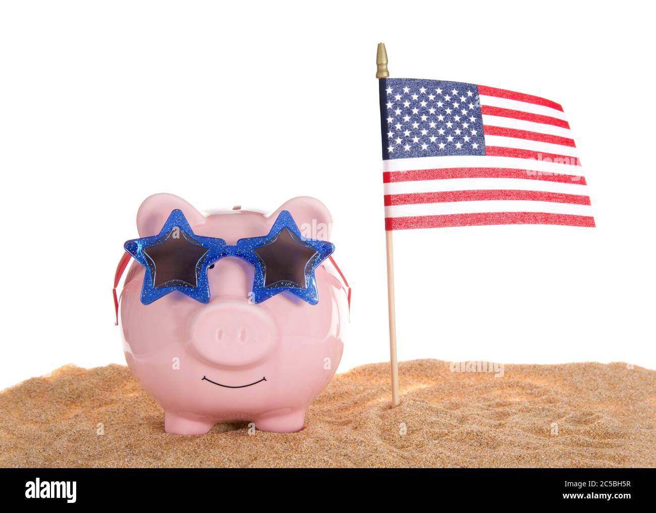 Traditional pink piggy bank wearing star glasses sitting in sand with American Flag waving, isolated on white. Stock Photo