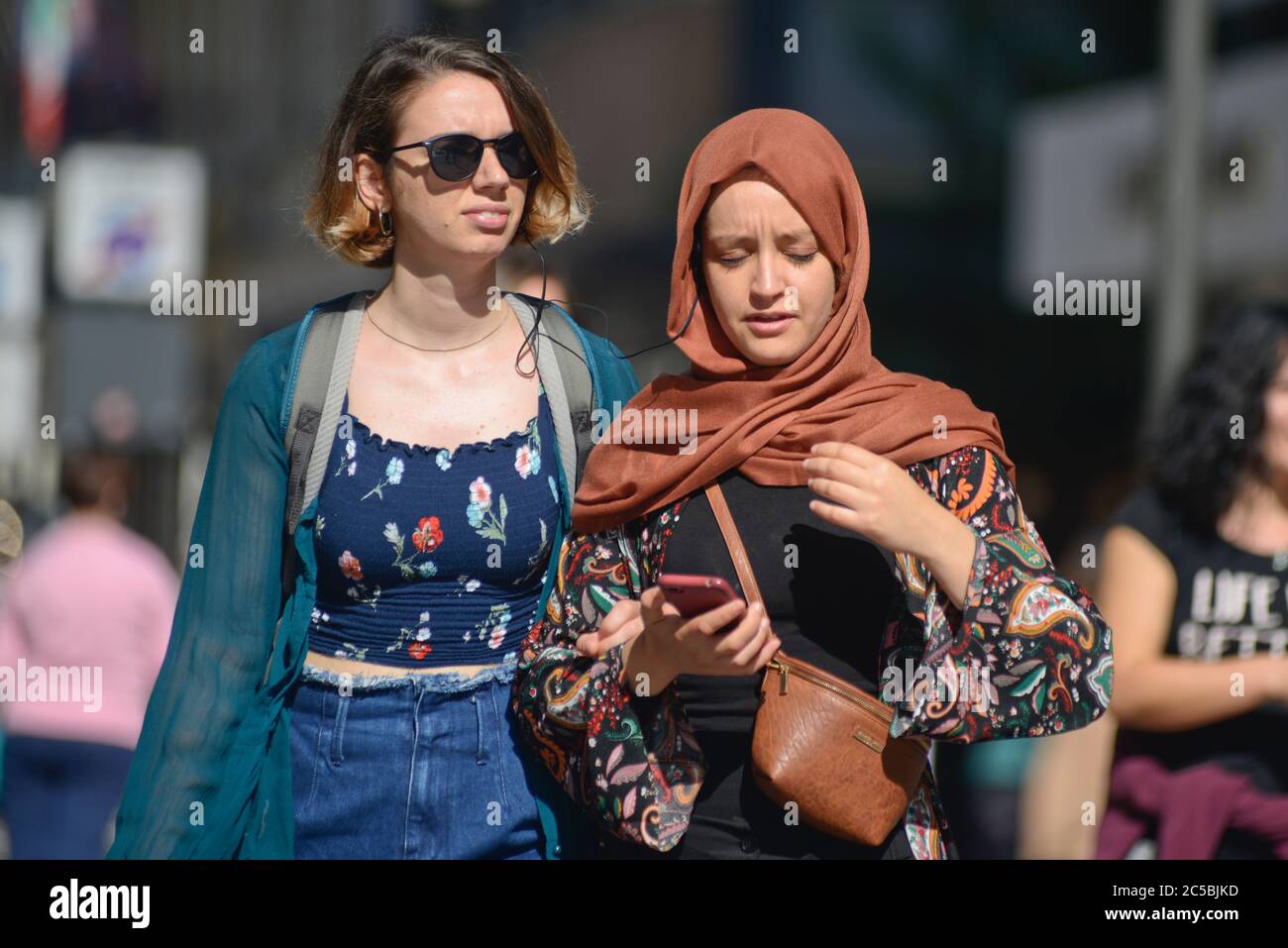 Italian young girls, one of them muslim, listening music togheter while walking in Via Sparano da Bari. Bari, Italy Stock Photo