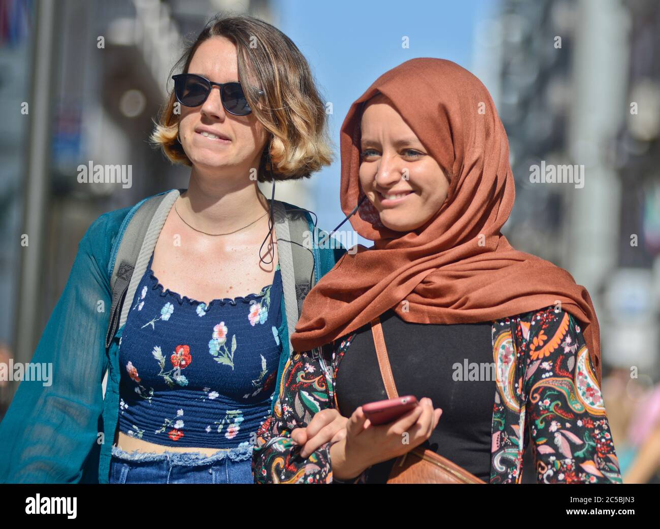 Italian young girls, one of them muslim, listening music togheter while walking in Via Sparano da Bari. Bari, Italy Stock Photo