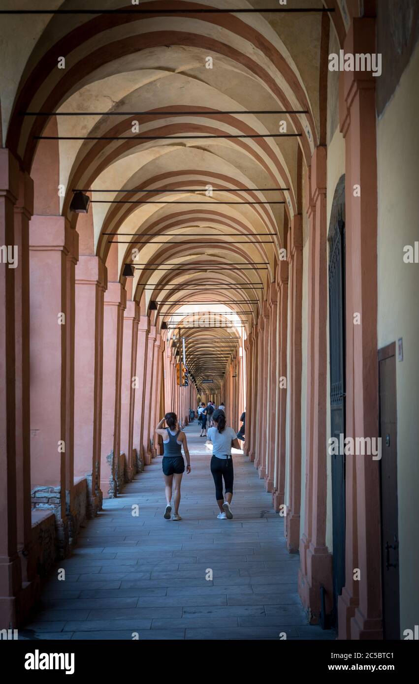Mother in black hat and daughter walking down promanade in sneakers and shorts and pants in Bologna Italy Stock Photo