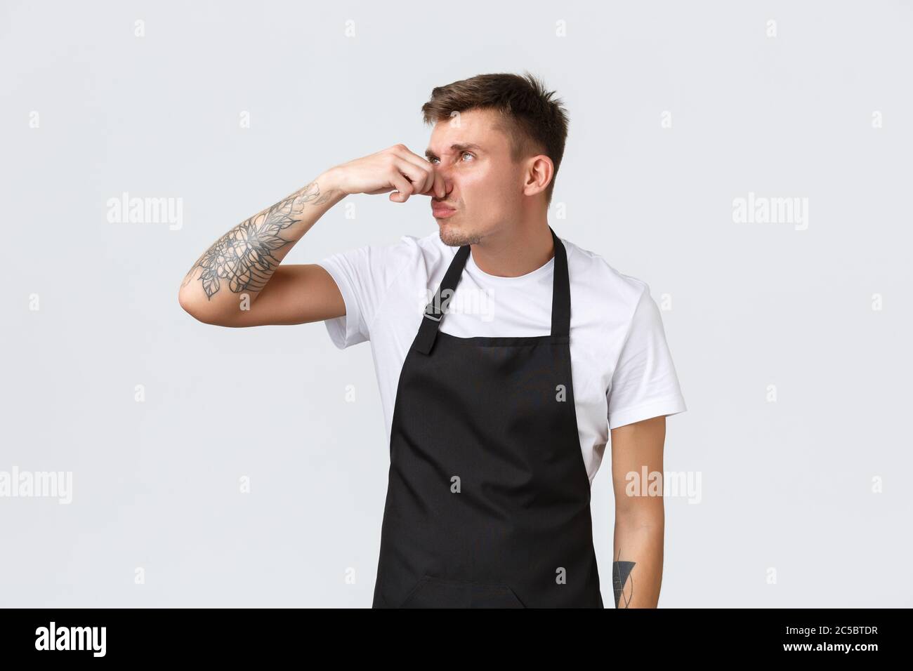 Employees, grocery stores and coffee shop concept. Annoyed and tired funny barista, cafe staff hates taking out stinky trash, shut nose and roll eyes Stock Photo