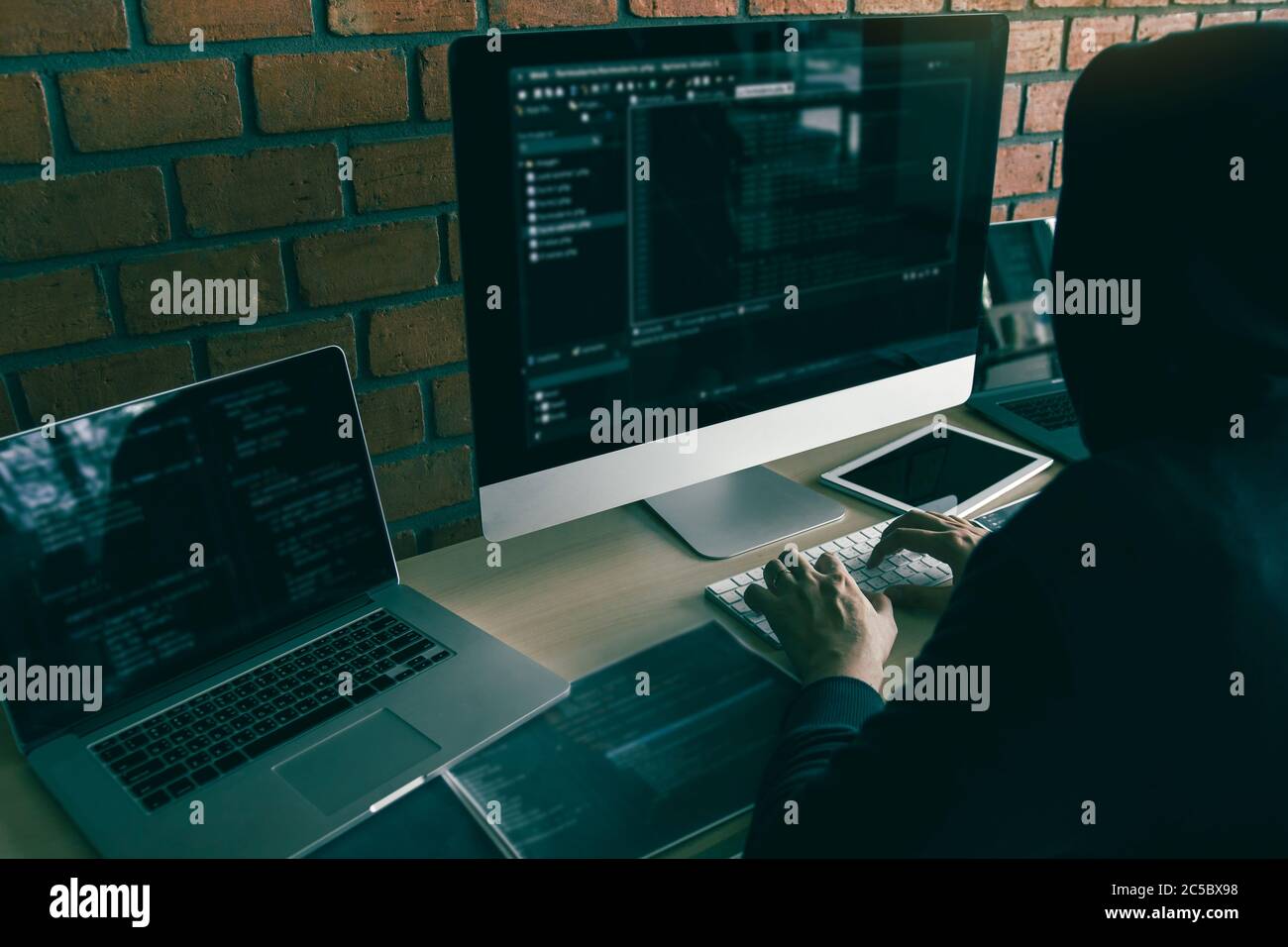 Hacker in the hood working with computer with hacking breaking into data servers. Stock Photo