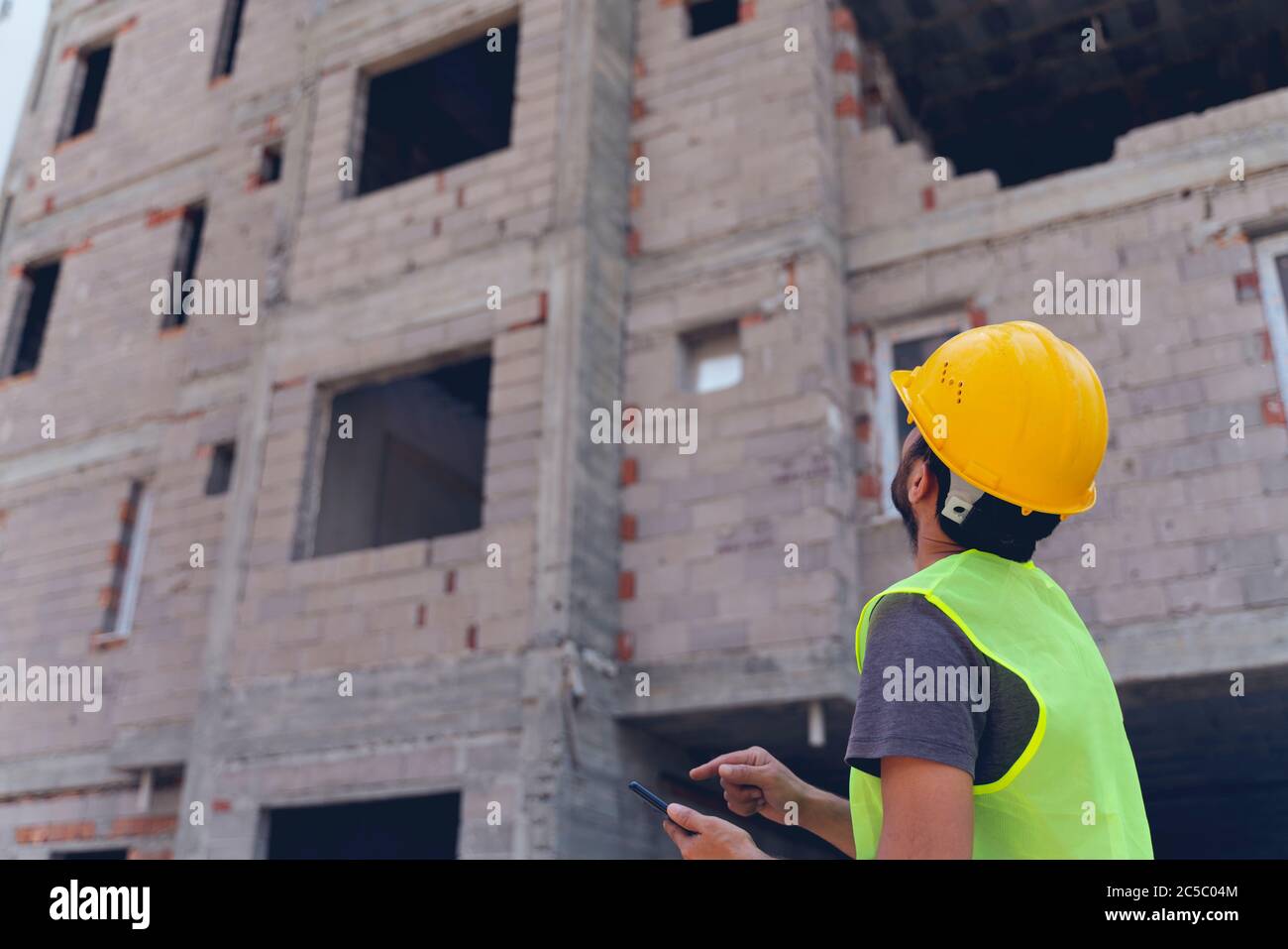 civil engineer or architect with hardhat on construction site checking schedule on smartphone Stock Photo