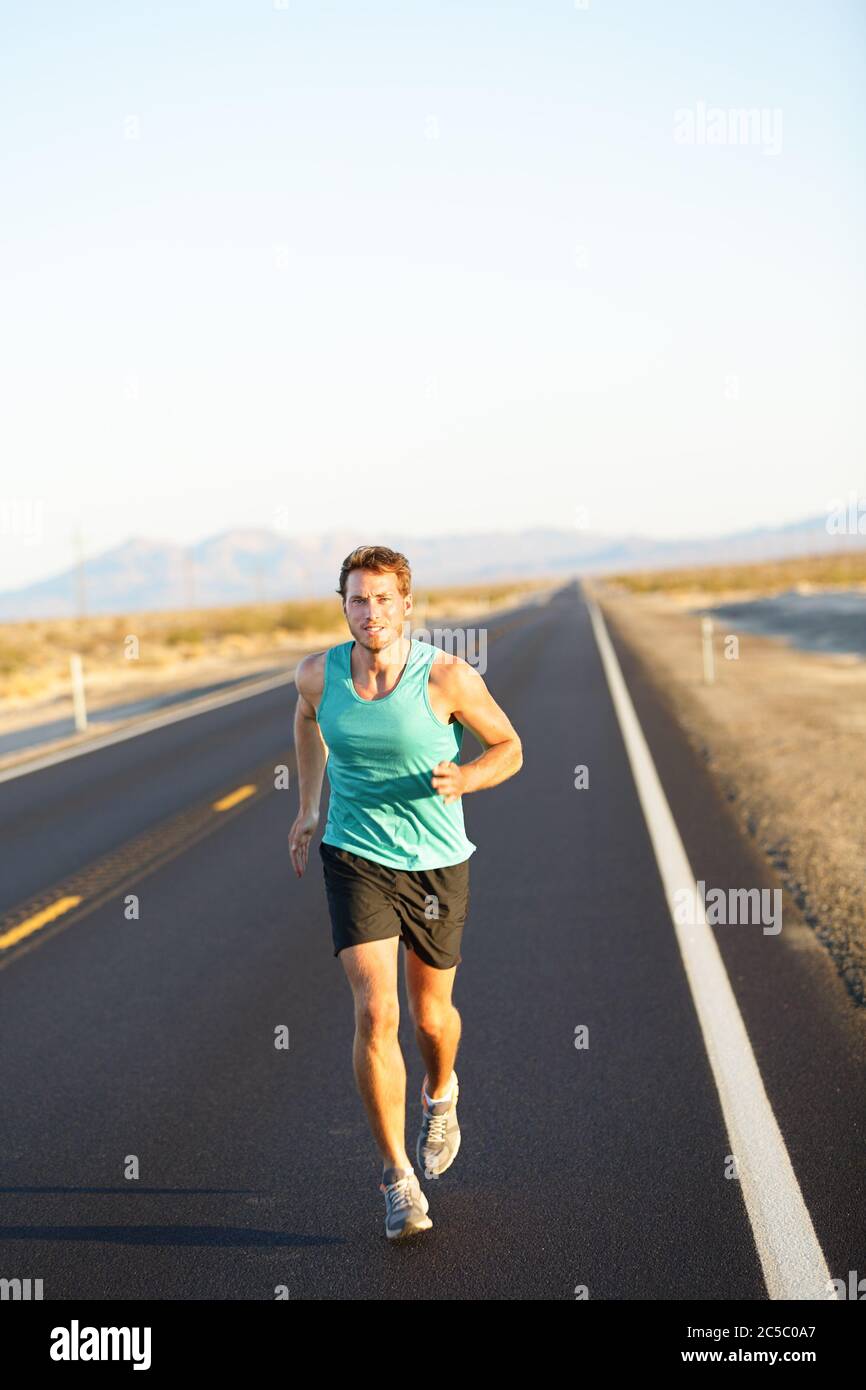 Male runner jogging and running on road in nature landscape. Fit fitness model man working out living healthy lifestyle training for marathon. Young caucasian model in his twenties. Stock Photo