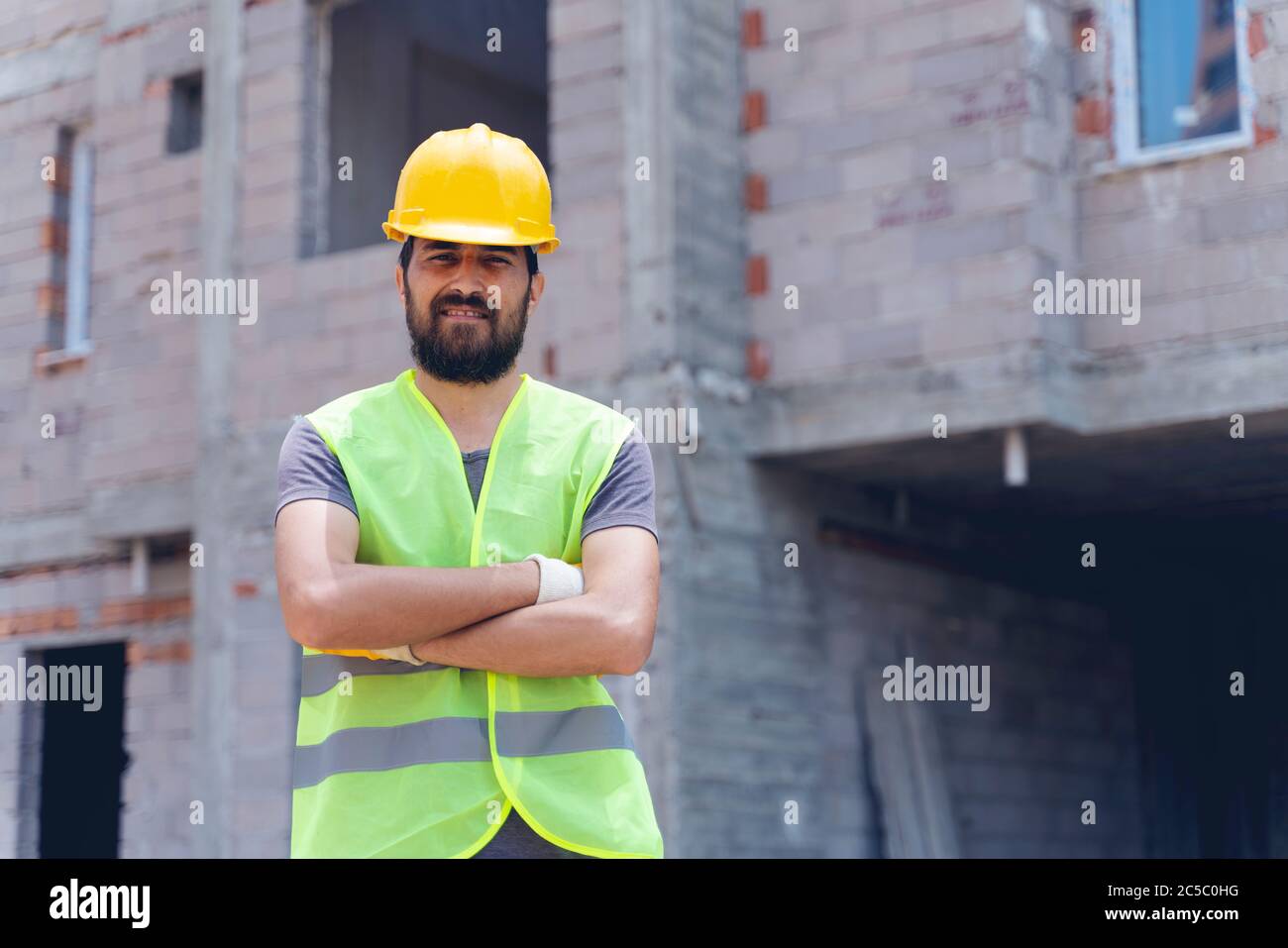 Construction worker looking at camera with hardhat in construction site background Stock Photo