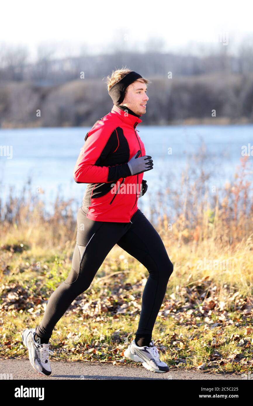 Running man jogging in autumn outdoor on cold day wearing long tights and sporty jogging outfit. Fit male fitness athlete model outdoor in fall. Full body length of jogger Stock Photo -