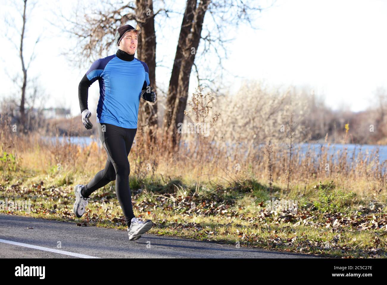 Male runner man running in autumn on cold day wearing long tights and long  sporty jogging outfit. Fit male fitness athlete model training outdoor in  fall. Full body length of jogger Stock