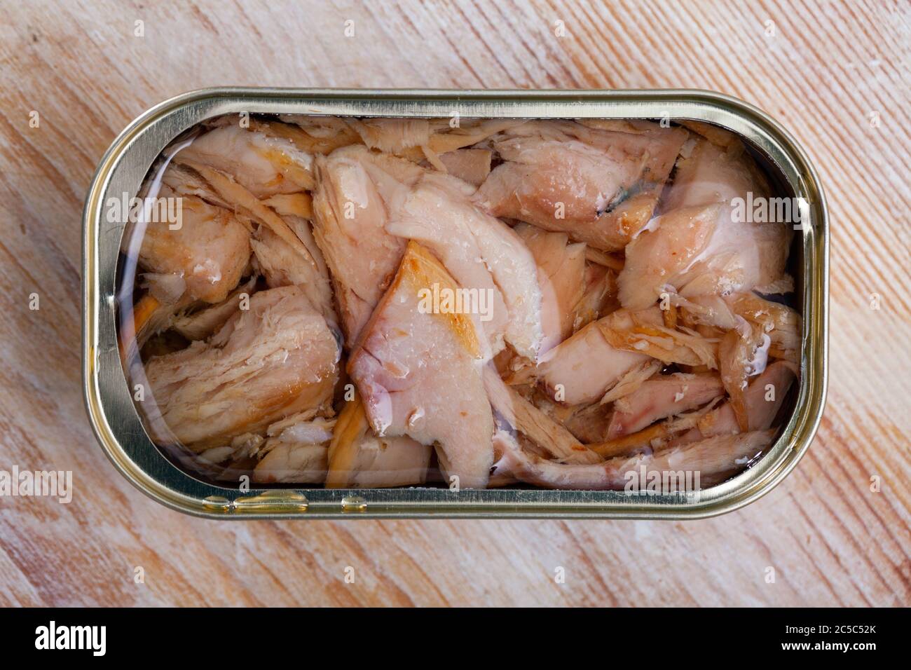 Open tin can of canned chopped tuna belly in oil on wooden table Stock
