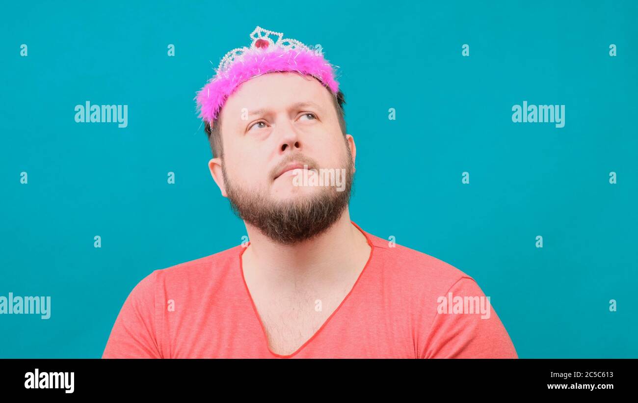 Playful bearded freaky man in a pink T-shirt with a deadema on his head sad with a magic wand in his hand. A funny wizard joke to make and fulfill a Stock Photo