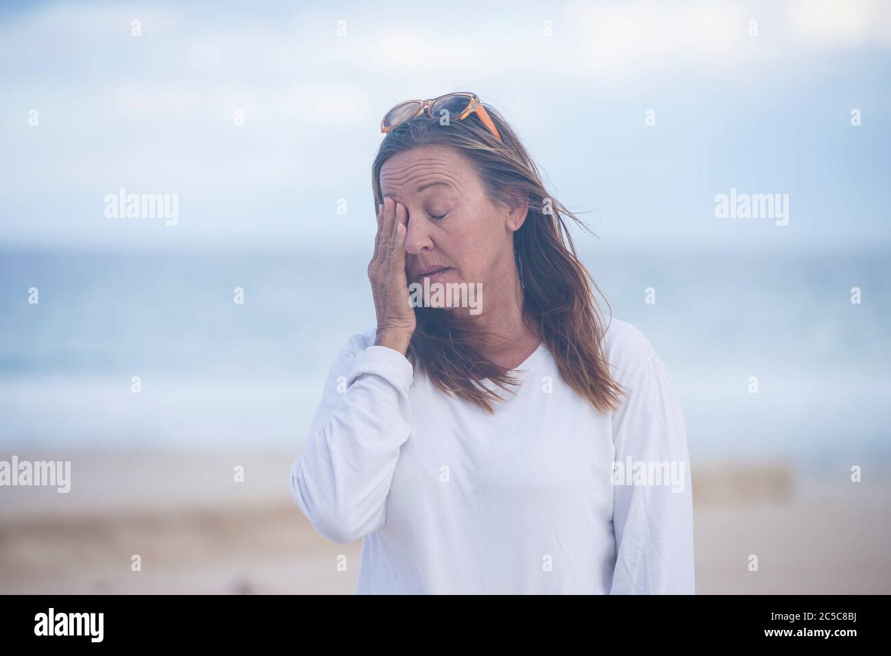 Portrait attractive mature woman with closed eyes, stressed, tired, sad, suffering from menopause, blurred background outdoor, copy space. Stock Photo