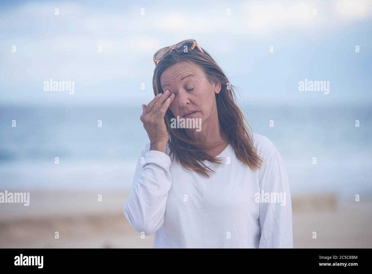 Portrait attractive mature woman with closed eyes, stressed, tired, suffering from menopause, blurred background outdoor, copy space. Stock Photo